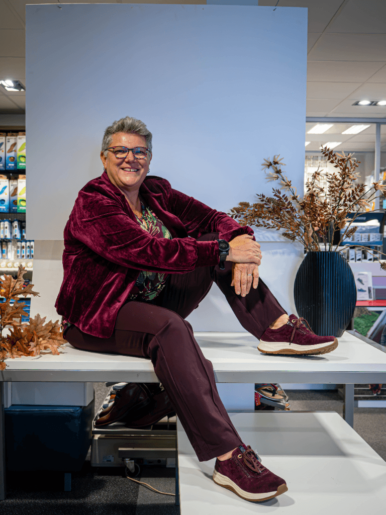 Helga zit in haar schoenenwinkel met een paar bordeauxrode schoenen aan